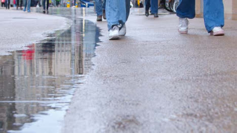 Pedestal-Shot-of-Rain-Falling-In-Puddle-as-Pedestrians-Walk-Past