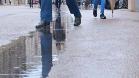 Pedestal-Shot-of-Rain-Falling-In-Puddle-as-People-Walk-Past