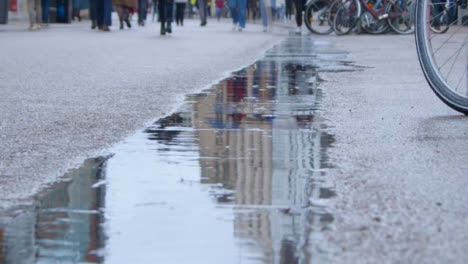 Tracking-Shot-Over-Puddle-as-Pedestrians-Walk-Past