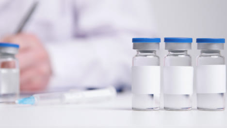 Close-Up-Shot-of-Medicine-Vials-with-Clean-White-Labels-as-Medical-Professional-Works-In-the-Background