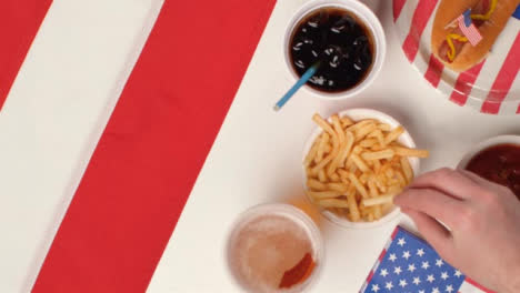 Top-Down-Shot-of-Hands-Taking-Fries-and-a-Beer-from-July-4th-Party-Food-Spread