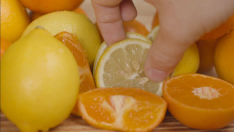 Close-Up-Shot-of-Hand-Taking-Slice-of-Lemon-Away-from-Pile-of-Citrus-Fruit