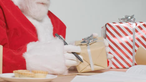 Mittlere-Aufnahme-Des-Weihnachtsmanns,-Der-Am-Schreibtisch-Sitzt-Und-Geschenke-Und-Geschenke-Organisiert