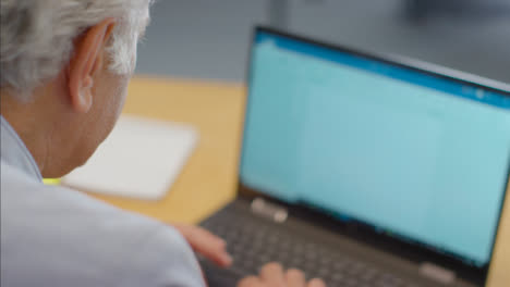 Over-the-Shoulder-Shot-of-Senior-Man-Typing-On-Laptop