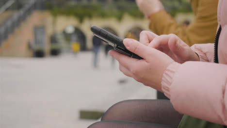Close-Up-of-Two-Women-Sitting-Outside-Using-Phones