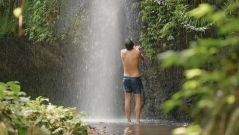 Mittlere-Aufnahme-Des-Rückens-Des-Mannes-Stand-Unter-Wasserfall-In-Bali