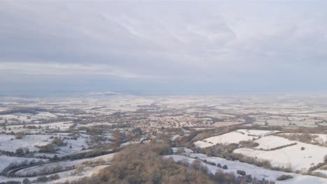 Drone-Shot-Rising-Above-Trees-Revealing-Snowy-Cotswold-Landscape