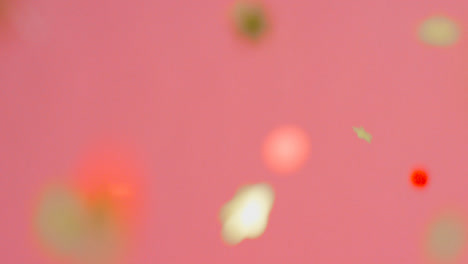 Stationary-Shot-of-Coloured-and-Gold-Confetti-Falling-Against-Bright-Pink-Background