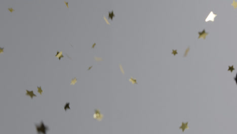 Stationäre-Aufnahme-Von-Goldenem-Sternkonfetti,-Das-Vor-Einem-Grauen-Hintergrund-Fällt