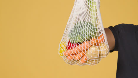 Mittenaufnahme-Eines-Mannes,-Der-Eine-Tüte-Gemüse-Vor-Gelbem-Hintergrund-Hochhält