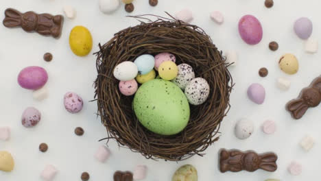 Ascending-Top-Down-Shot-of-Rotating-Easter-Confectionary-In-a-Nest