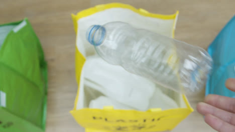 Von-Oben-Nach-Unten-Ziehen-Sie-Den-Fokus-Einer-Person,-Die-Eine-Plastikflasche-In-Einen-Recyclingbeutel-Wirft