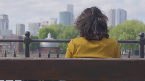 Panning-Mid-Shot-of-Woman-Sitting-on-Bench-Looking-at-City-Skyline