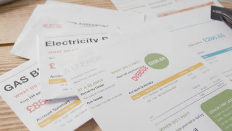 Close-Up-Of-Man-Opening-Overdue-UK-Utility-Bills-And-Adding-To-Pile-On-Table