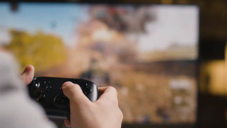 Close-Up-Hands-As-Man-Plays-With-Video-Game-Controller-Screen-In-Background