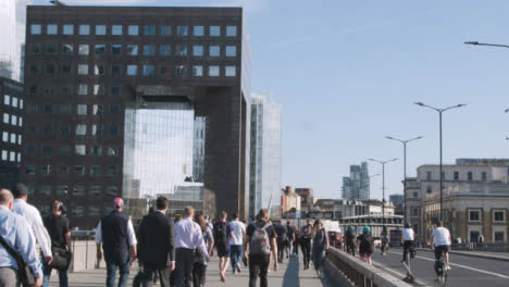 Commuters-Walking-Across-London-Bridge-With-Office-Buildings-In-Background