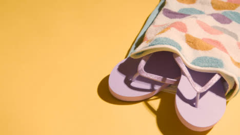 Summer-Holiday-Vacation-Concept-Of-Flip-Flops-Sandals-Beach-Towel-On-Yellow-Background