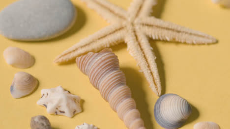 Summer-Holiday-Concept-Of-Rotating-Shells-Pebbles-Starfish-On-Yellow-Background