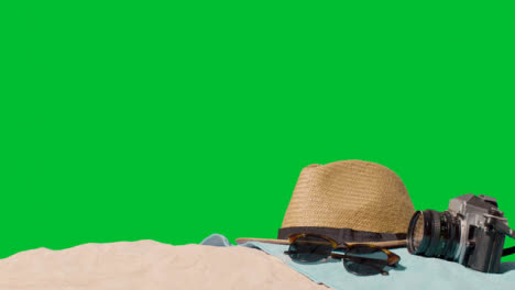 Summer-Holiday-Concept-Of-Sunglasses-Sun-Hat-Camera-Beach-Towel-On-Sand-Against-Green-Screen