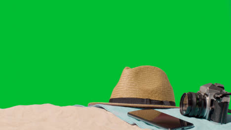 Summer-Holiday-Concept-Of-Camera-Mobile-Phone-Sun-Hat-Beach-Towel-On-Sand-Against-Green-Screen-2