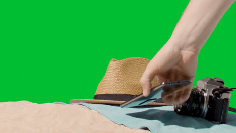 Summer-Holiday-Concept-Of-Camera-Sun-Hat-Mobile-Phone-Beach-Towel-On-Sand-Against-Green-Screen-4