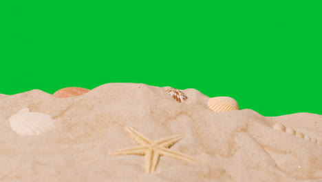 Summer-Holiday-Concept-With-Shells-Starfish-On-Sandy-Beach-In-Foreground-Against-Green-Screen-1