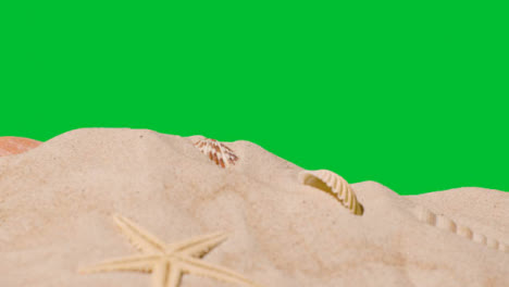 Summer-Holiday-Concept-With-Shells-Starfish-On-Sandy-Beach-In-Foreground-Against-Green-Screen-2