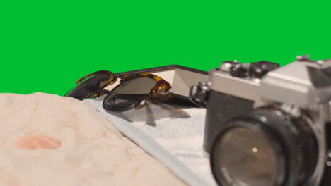 Summer-Holiday-Concept-Of-Book-Camera-Beach-Towel-On-Sand-Against-Green-Screen-1