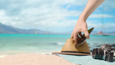Summer-Holiday-Concept-Of-Camera-Sun-Hat-Mobile-Phone-Beach-Towel-On-Sand-Against-Sea-3