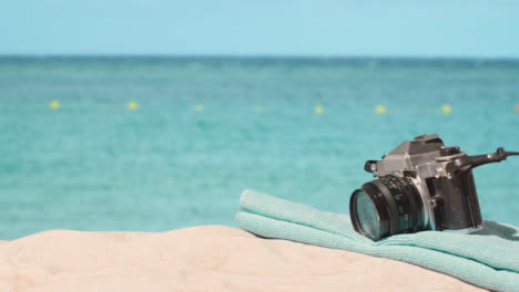 Summer-Holiday-Concept-Of-Person-Picking-Up-Camera-Beach-Towel-On-Sand-Against-Sea-Background