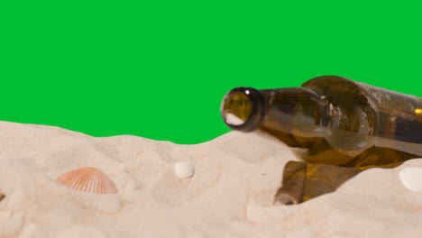 Pollution-Concept-With-Hand-Dropping-Bottle-On-Beach-Against-Green-Screen