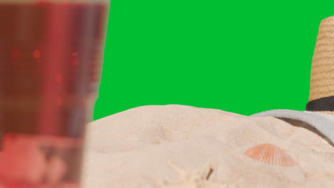 Summer-Holiday-Concept-Of-Cold-Drink-On-Beach-Towel-With-Sun-Hat-Against-Green-Screen-1