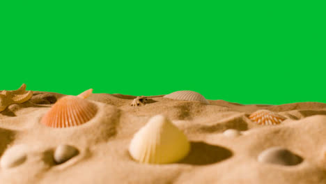 Summer-Holiday-Concept-With-Shells-Starfish-On-Sandy-Beach-In-Foreground-Against-Green-Screen