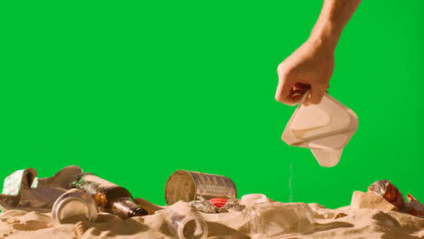 Pollution-Concept-With-Hand-Picking-Up-Bottles-And-Rubbish-On-Beach-Against-Green-Screen