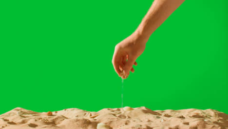 Summer-Holiday-Concept-With-Hand-Picking-Up-Shells-Starfish-On-Sandy-Beach-Against-Green-Screen