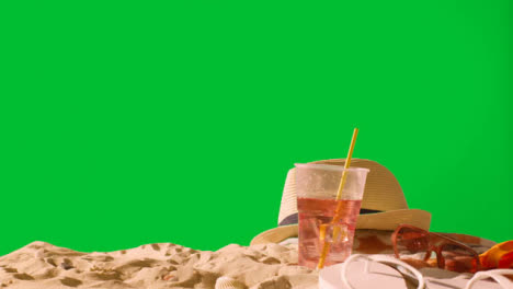 Summer-Holiday-Concept-Of-Cold-Drink-On-Beach-Towel-With-Flip-Flops-Sunglasses-And-Sun-Hat-Against-Green-Screen