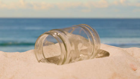 Pollution-Concept-With-Glass-Jar-Being-Thrown-Onto-Beach-Against-Sea-Background