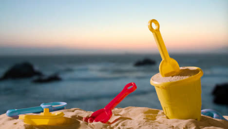 Summer-Holiday-Concept-With-Child's-Bucket-Spade-On-Sandy-Beach-Against-Sea-And-Sunset-Sky