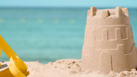 Summer-Holiday-Concept-With-Child's-Bucket-Spade-And-Sandcastle-On-Sandy-Beach-Against-Sea