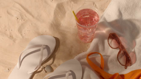 Summer-Holiday-Concept-Of-Cold-Drink-Sunglasses-Beach-Towel-Flip-Flops-Swimsuit-On-Sand-2