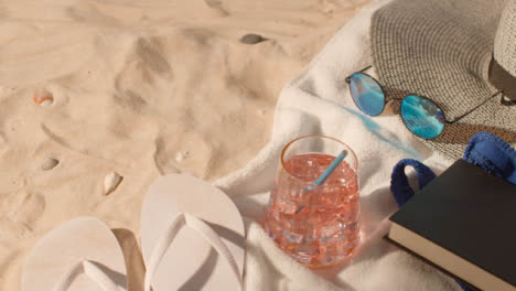 Summer-Holiday-Concept-Of-Cold-Drink-Sunglasses-Beach-Towel-Flip-Flops-Hat-Book-On-Sand-1