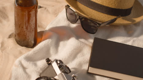 Summer-Holiday-Concept-Of-Beer-Bottle-Sunglasses-Beach-Towel-Book-Sun-Hat-Camera-On-Sand-3