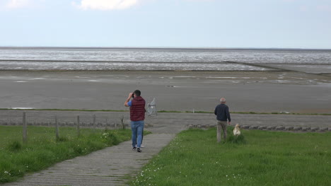 Germany-Wadden-Sea-people-walk-down-dike-with-dog-at-low-tide