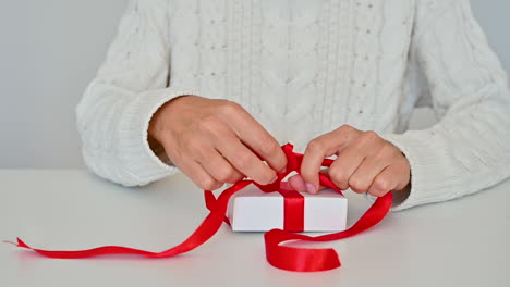 Weibliche-Hände-Binden-Die-Rote-Schleife-Einer-Geschenkbox-Mit-Weißer-Verpackung