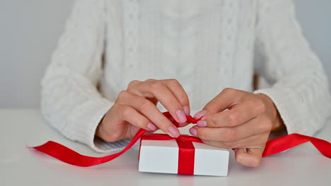 Nahaufnahme-Weibliche-Hände-Binden-Die-Rote-Schleife-Einer-Geschenkbox-Mit-Weißer-Verpackung