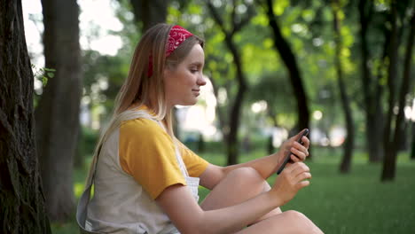 Mujer-Muy-Joven-Usando-Su-Teléfono-Inteligente-En-Un-Parque-Verde
