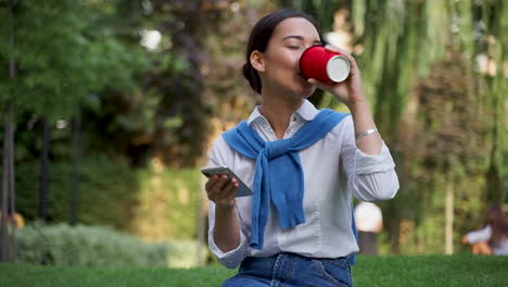 Woman-Reading-Messages-On-Her-Phone-And-Drinking-A-Coffee-Outdoors