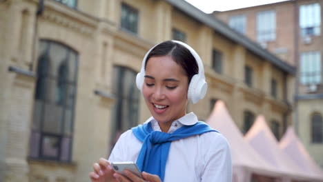 Cheerful-Woman-Listening-To-Music-With-Headphones-And-Walking-Down-The-Street