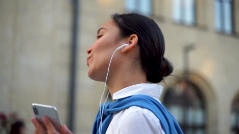 Cheerful-Woman-Listening-To-Music-With-Earphones-And-Walking-Down-The-Street