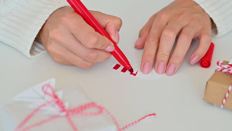 Female-Hands-Decorate-The-Bow-Of-A-Wrapped-Christmas-Gift-With-A-Paper-Tree